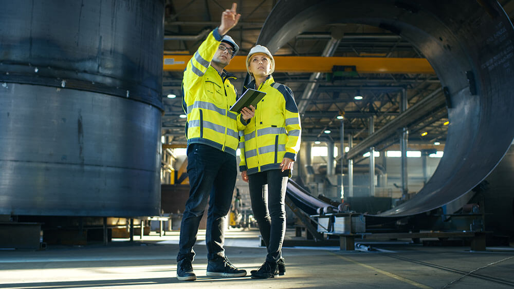 Male and Female Industrial Engineers in Hard Hats Discuss New Project while Using Tablet Computer.