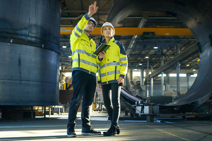 Male and Female Industrial Engineers in Hard Hats Discuss New Project while Using Tablet Computer.